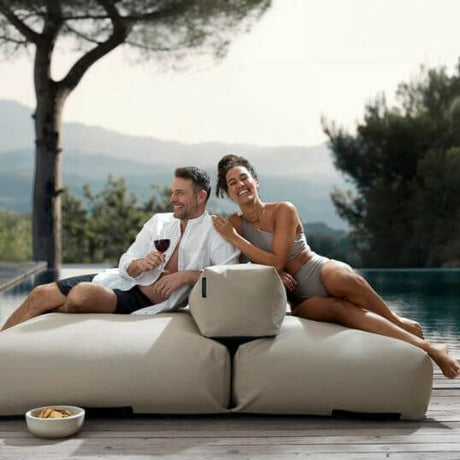 Ein Paar sitzt auf einem Poolsofa Double, beide lehnen sich in der Mitte an die flexibel positionierbare Rückenlehne. sie lachen und genießen das bequeme Sitzen.